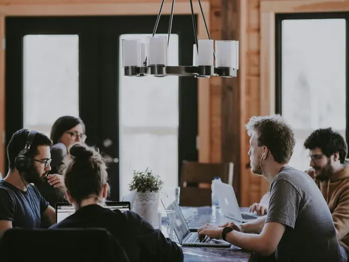 Group of young professionals collaborating at a table with laptops and headphones, representing coworking services in listings
